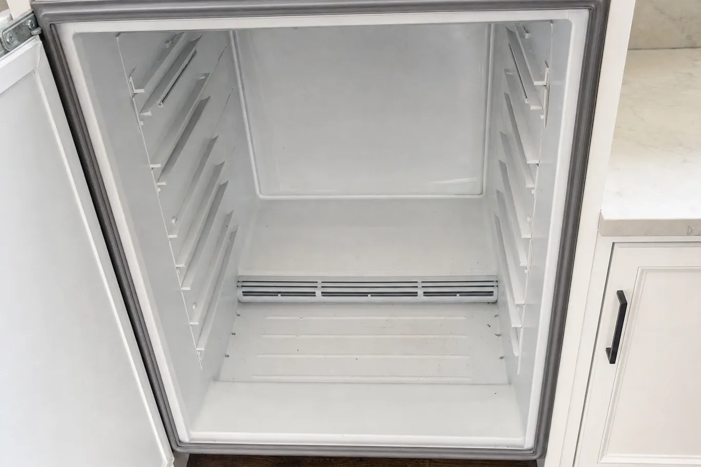 An empty undercounter refrigeration cabinet with a thick grey magnetic gasket around the door opening and a wide vent grille across the floor at the back