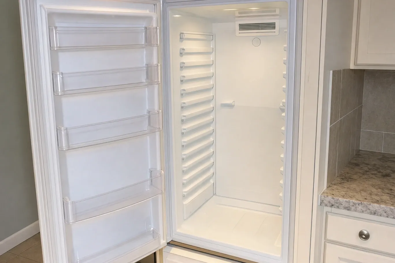 A full-height refrigerator column standing open and empty, clear bins on the door and a ladder of shelf supports down both walls of the white liner
